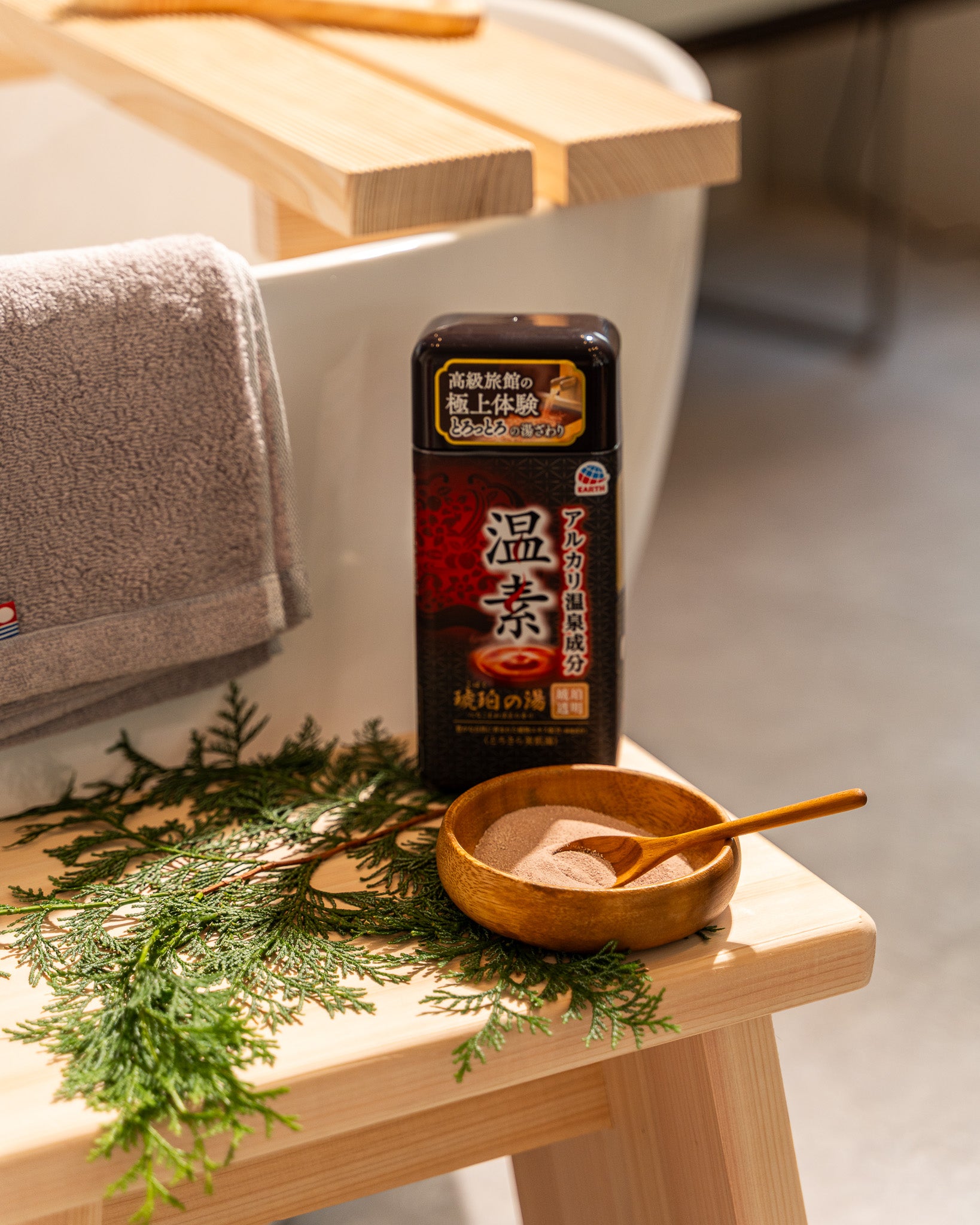 Bath salt packaging with a wooden bowl and spoon on a wooden bench with greenery