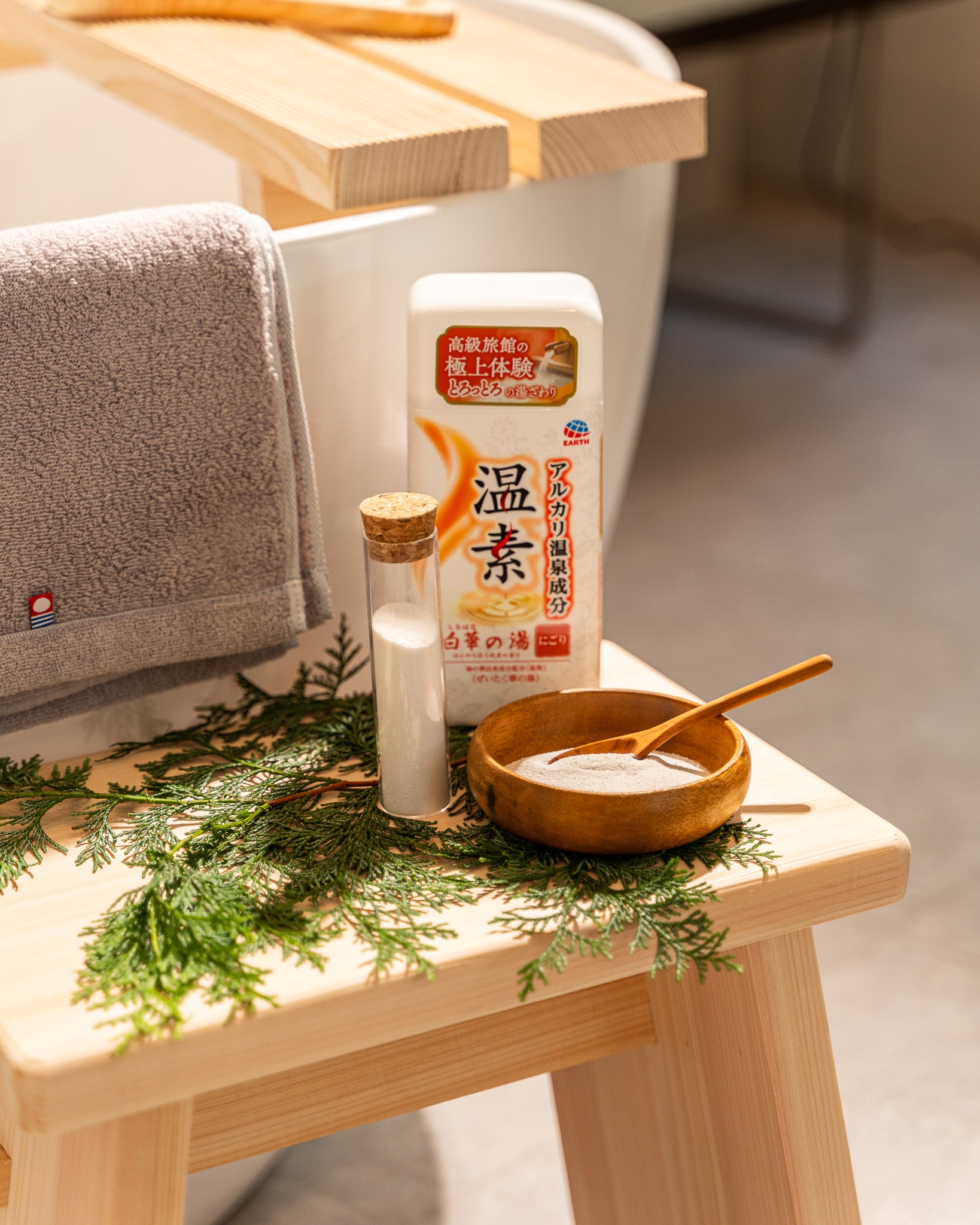 Bowl with a wooden spoon, bottle, and towel on a wooden stool with a blurred background