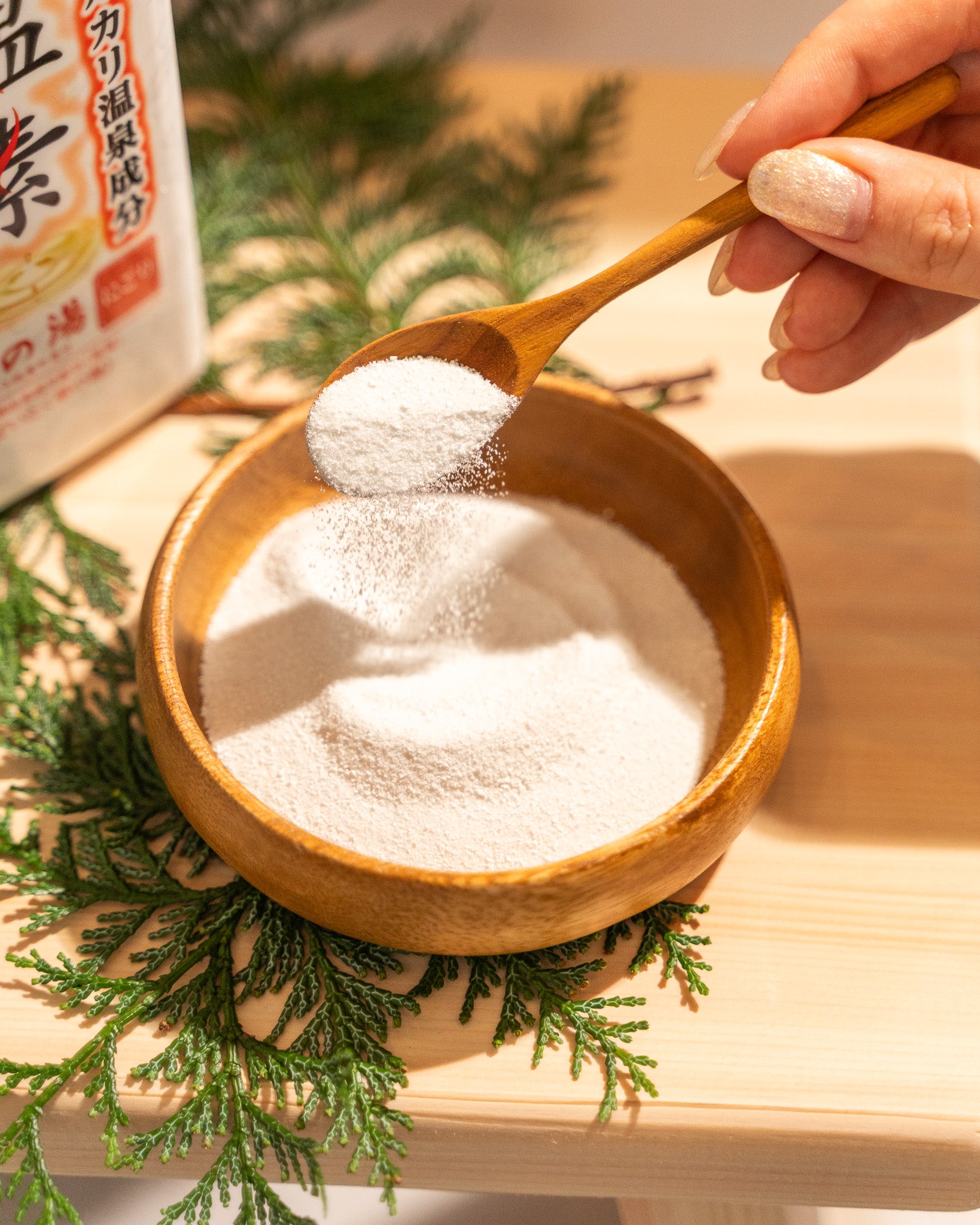 Wooden spoon with white powder over a wooden bowl on a wooden surface with greenery