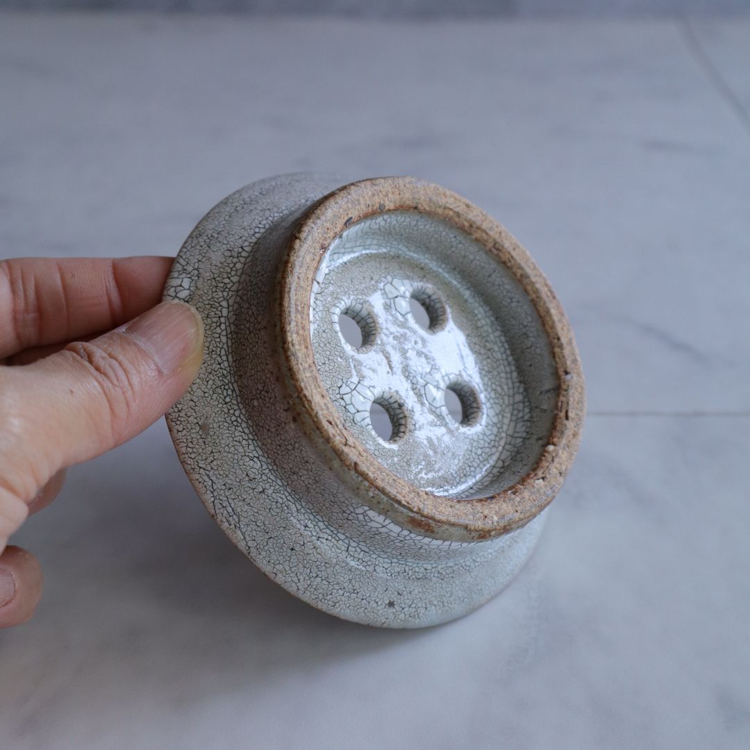 The underside of the ceramic soap dish showing raw clay base and drainage hole design with visible crackled glaze
