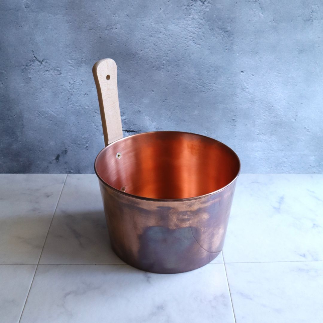 Side view of a handmade Japanese copper sauna bucket with a natural beechwood handle, showing its smooth bronze finish.