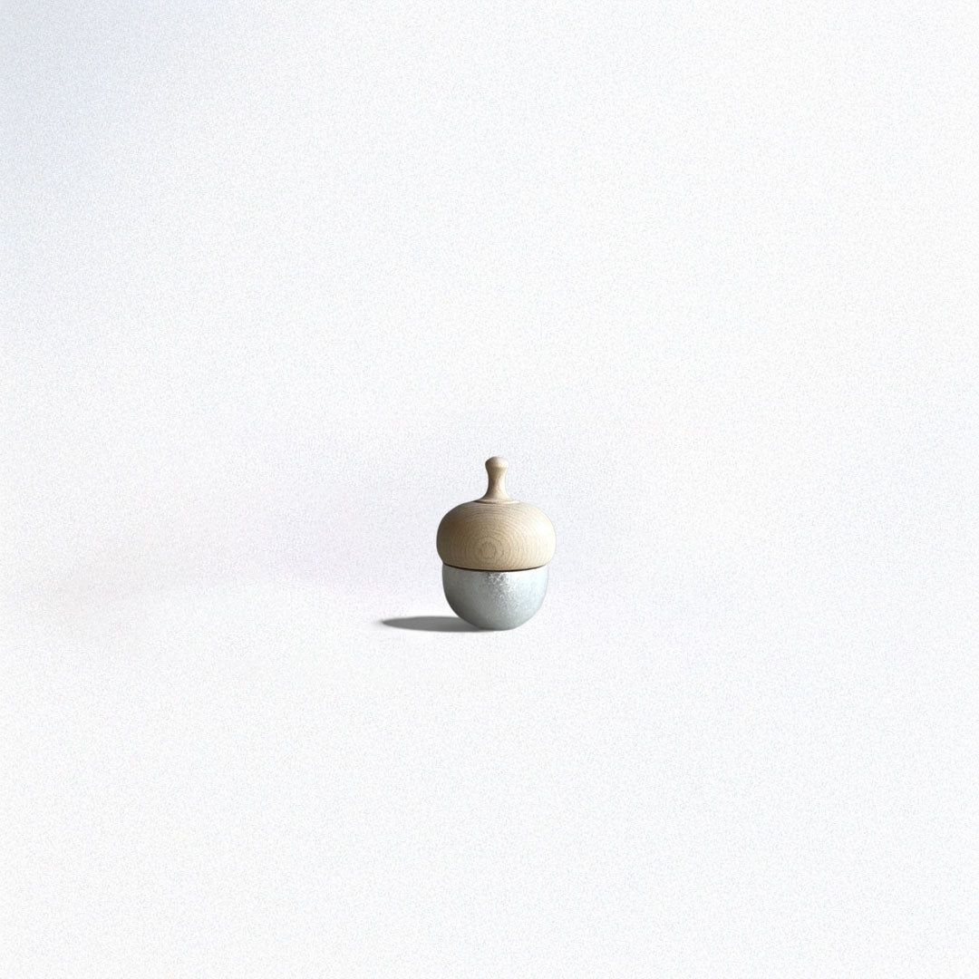 A small acorn-shaped healing bell with a silver base and a wooden top, placed on a smooth surface against a soft, neutral background.