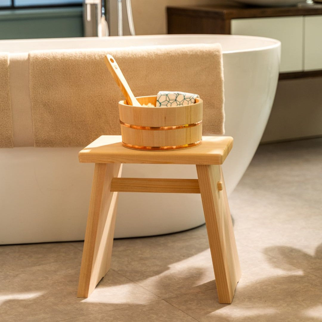 Wooden bath stool with a basket containing items next to a bathtub in a bathroom setting.