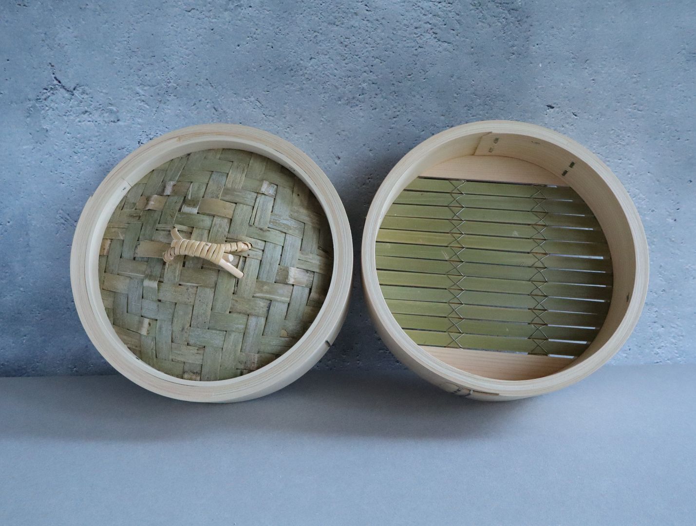 Two parts of a bamboo steamer against a grey wall
