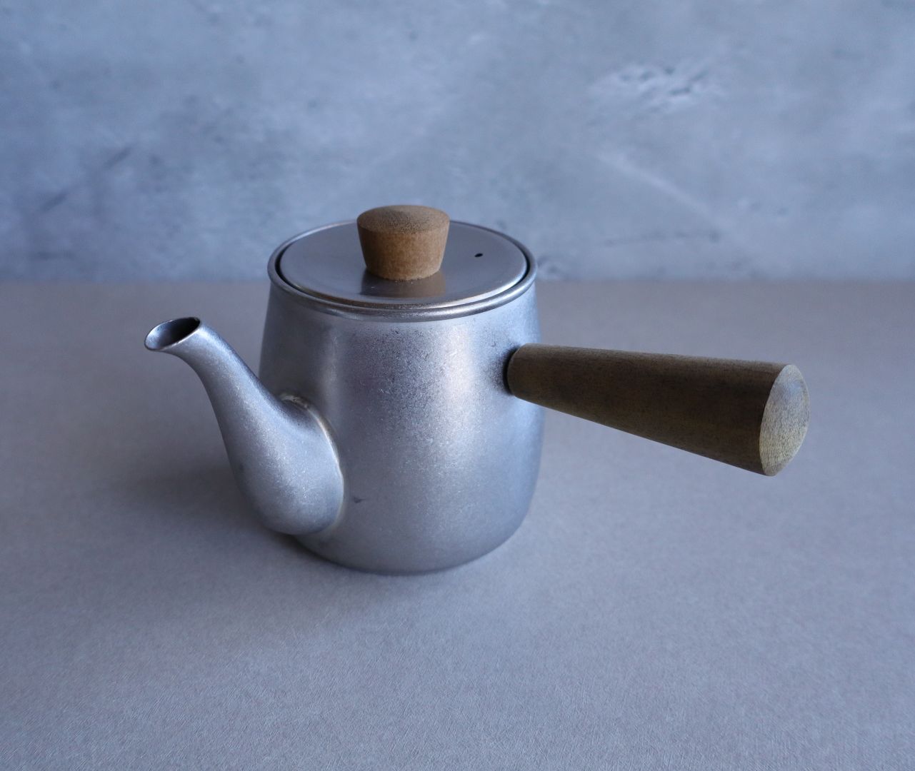A compact Japanese-style teapot made of stainless steel with a side wooden handle and wooden knob on the lid