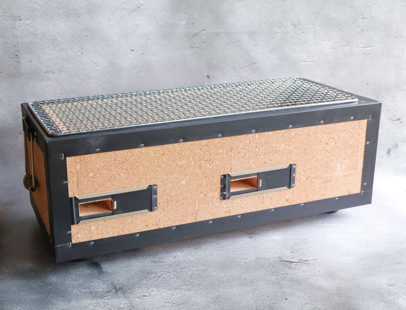 A side view of a Japanese rectangular hibachi grill featuring cork insulation and metal framing with a wire grilling surface.