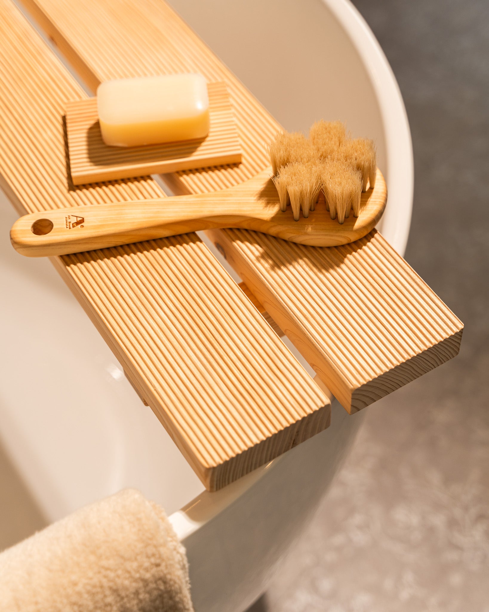 Wooden bath brush, scrubber, and soap on a wooden tray with a neutral background