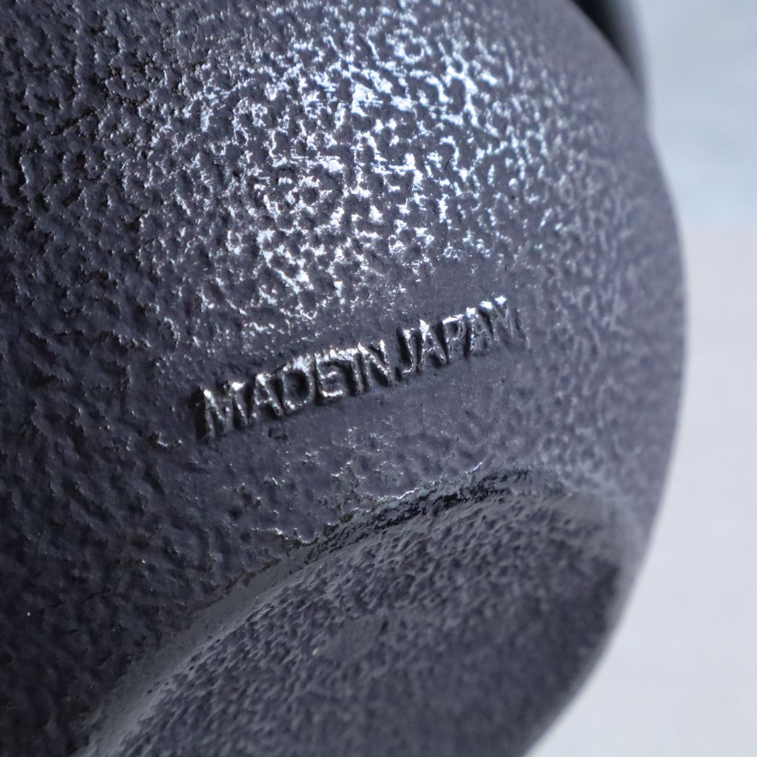 Close-up of the bottom of a black cast iron teapot showing the embossed 'MADE IN JAPAN' mark on its textured surface.