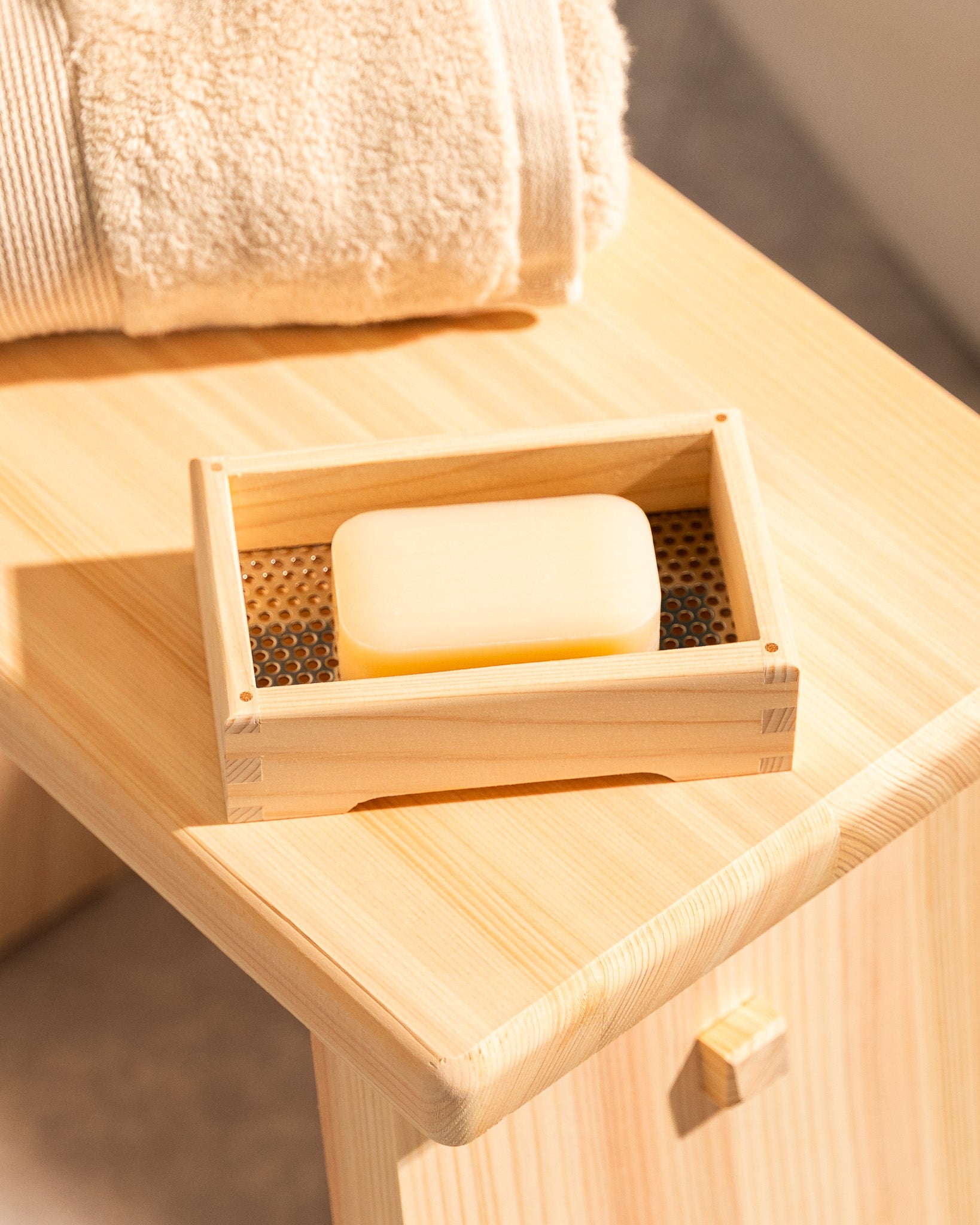 Wooden soap dish with a bar of soap on a wooden surface with a towel in the background