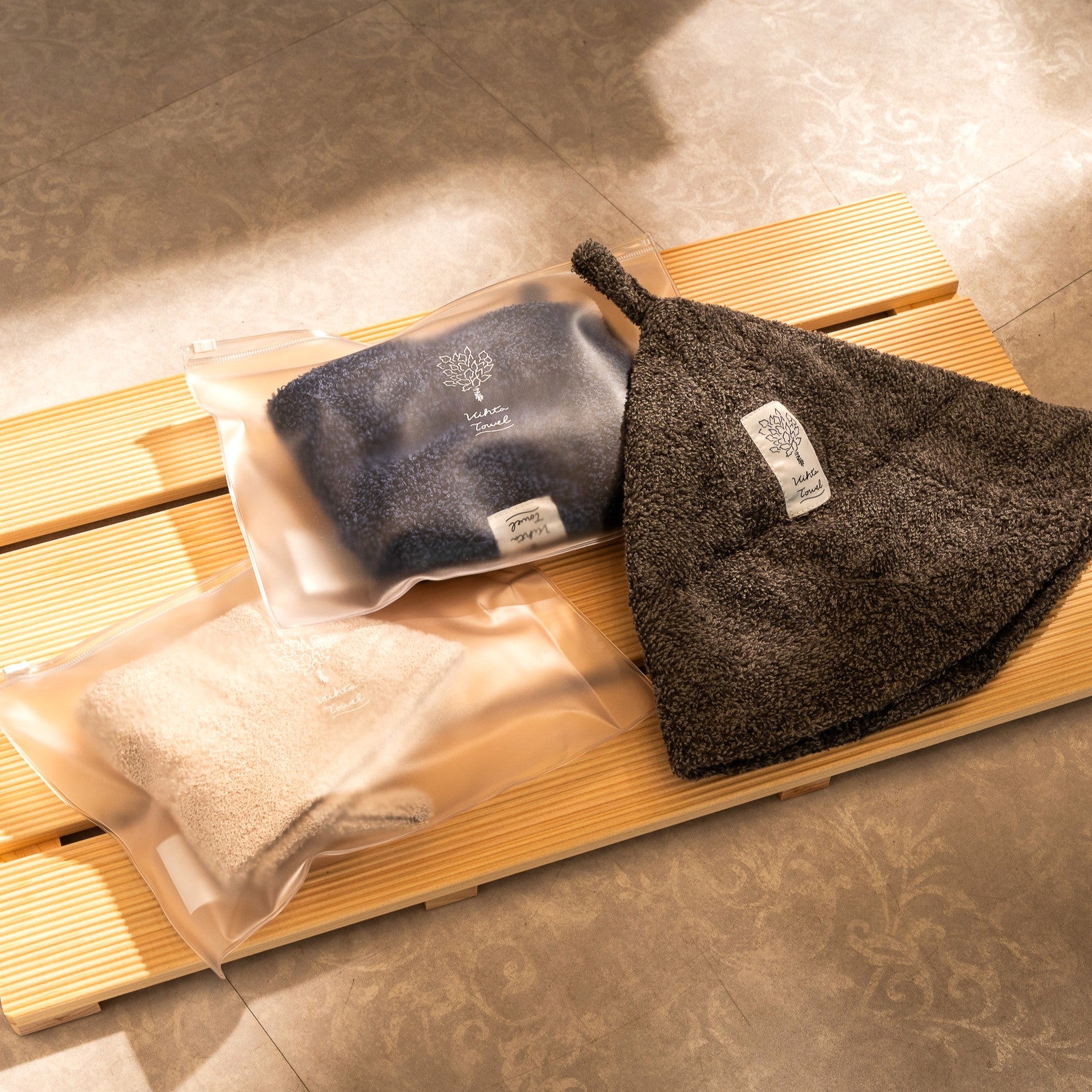 Navy, beige, and charcoal sauna hats displayed with frosted waterproof zipper pouches on a wooden bench.