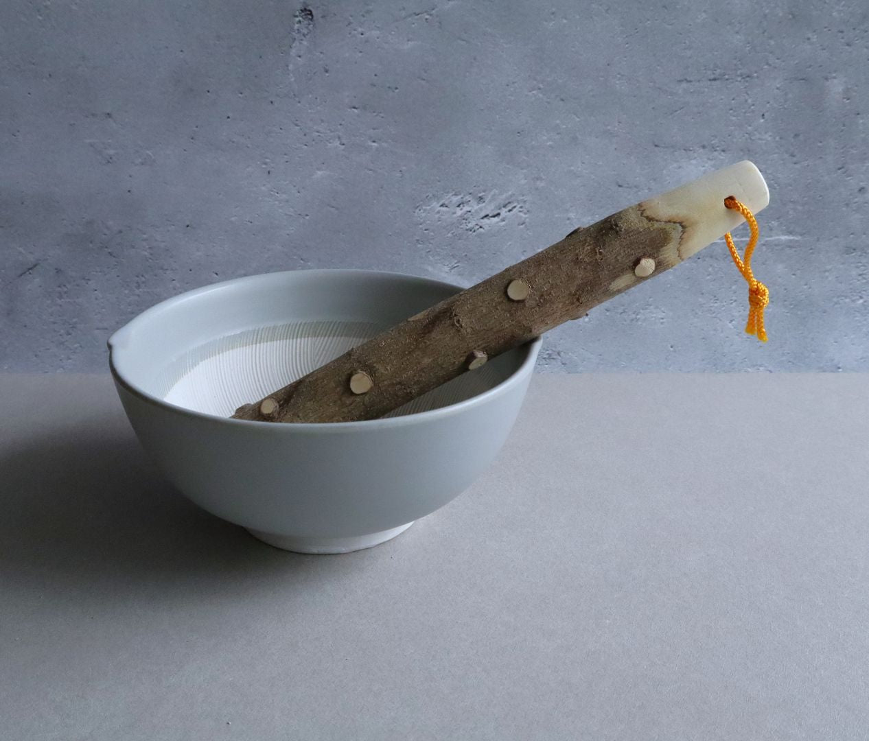 A suribachi bowl made in ceramic with a wood pestle in a grey room