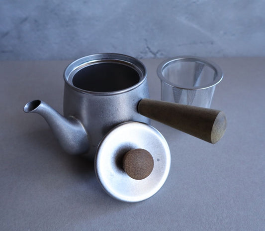 Stainless steel teapot with its lid removed and a fine mesh tea strainer placed beside it