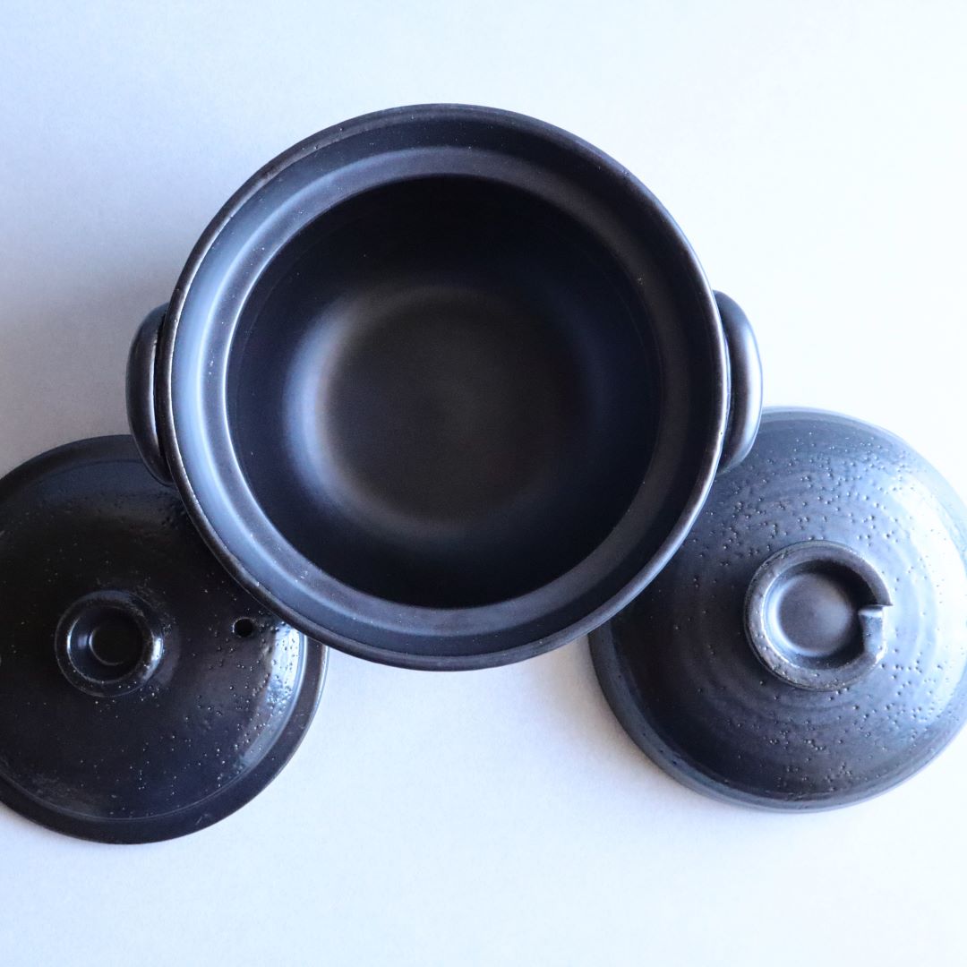 Top view of a black glazed donabe rice cooker with its components, including the lid and inner pot, arranged separately. The cooker is designed for optimal heat retention and delicious rice cooking.