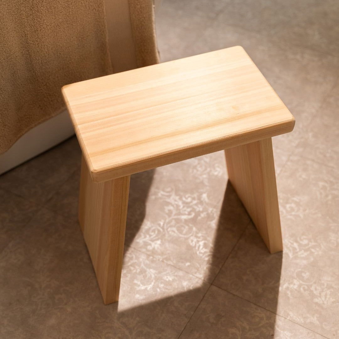 Wooden bathroom stool on a tiled floor with a towel in the background