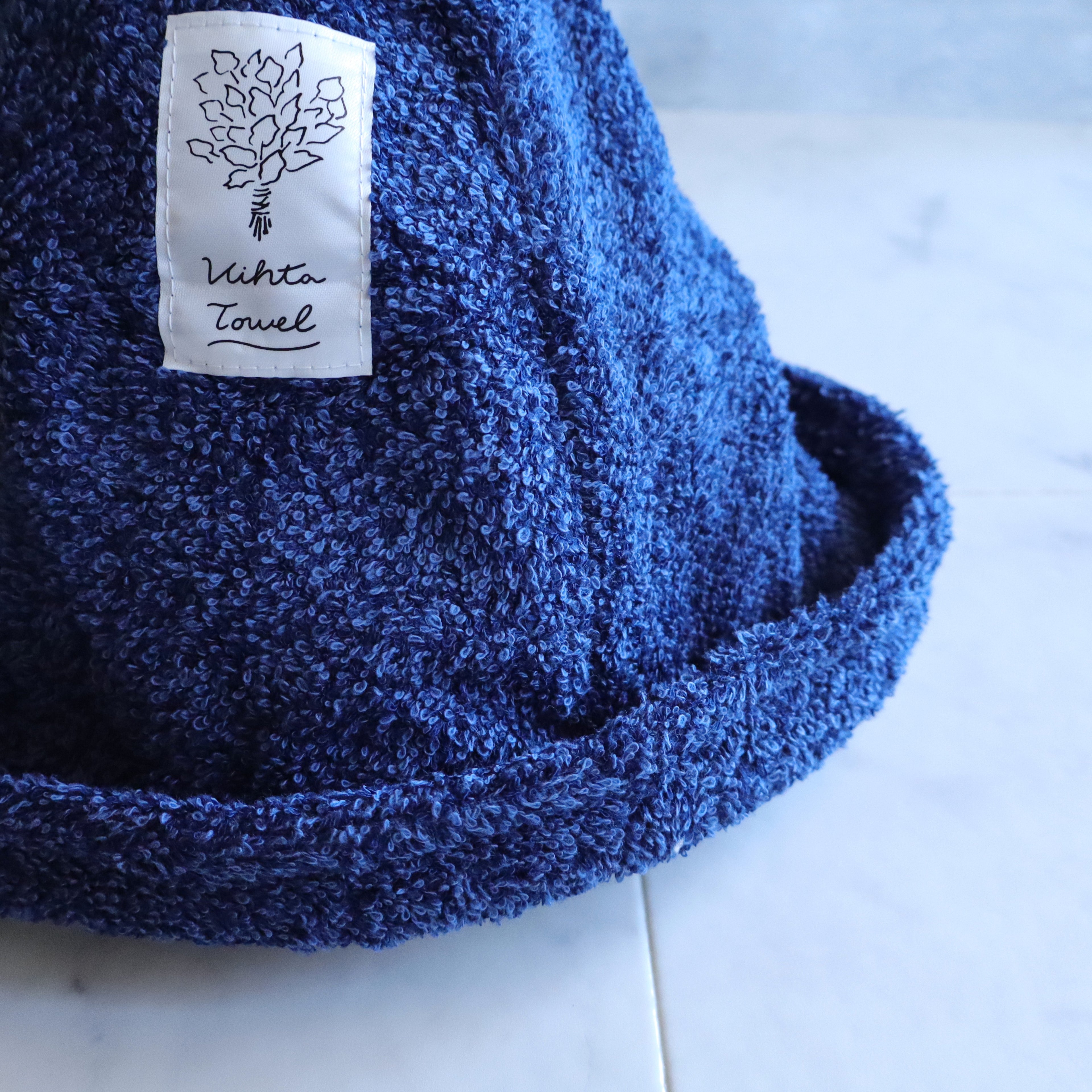 Close-up of the navy sauna hat showing the Vihta Towel label, soft terry texture, and foldable brim.