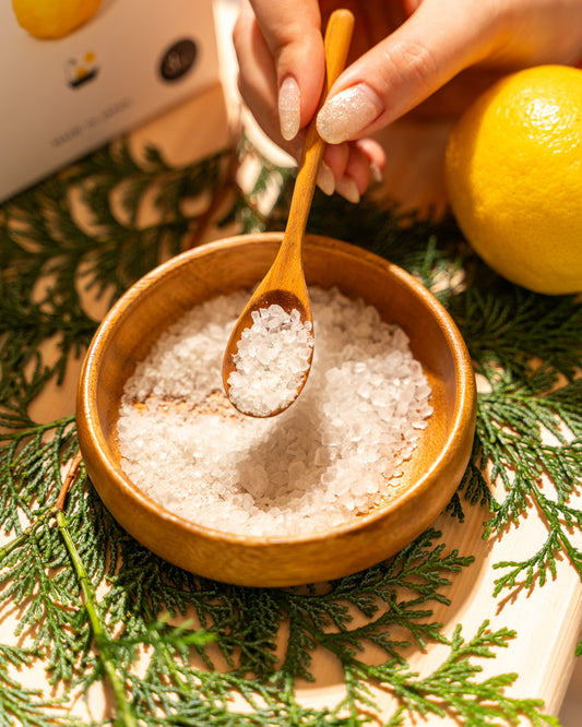Wooden bowl with sea salt, wooden spoon, and lemon on a green leafy background
