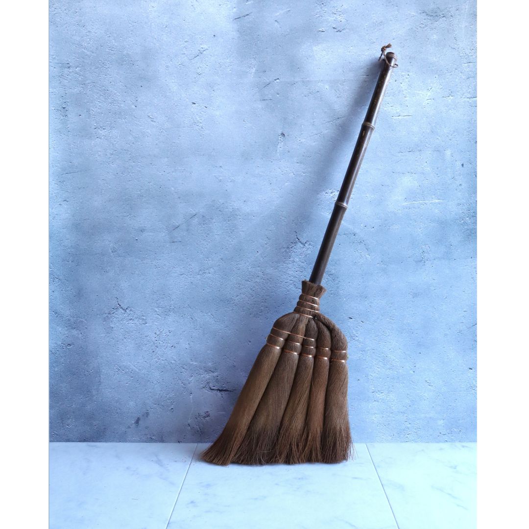 a traditional Japanese palm broom made of natural hemp palm bark, standing upright in the middle of a grey room.