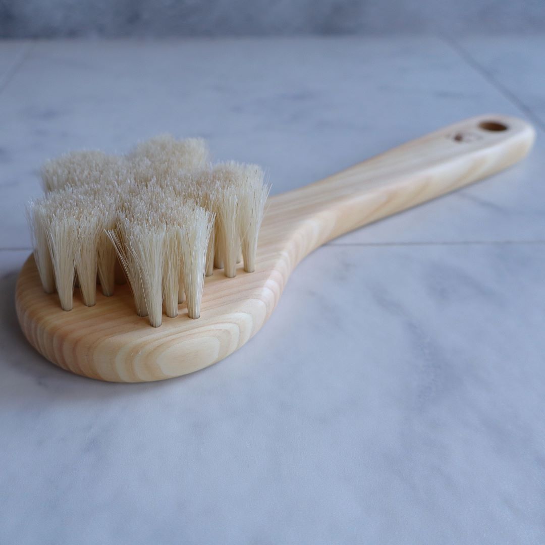 Close-up of a Japanese Sakura body brush made from natural Hinoki wood, featuring soft white horsehair bristles shaped like a cherry blossom, designed for gentle exfoliation and spa-like skincare.