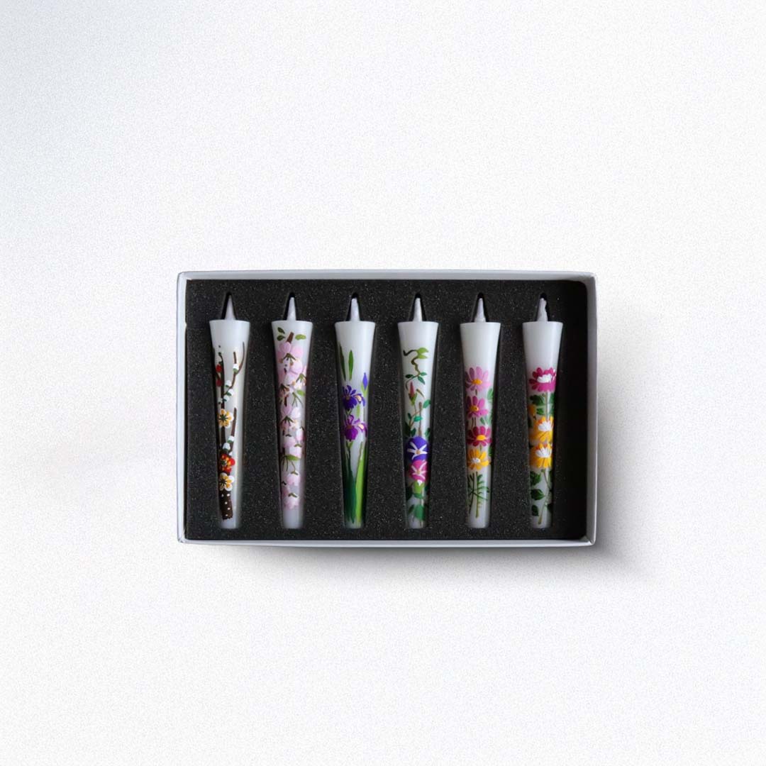 Set of six floral-patterned candles in a black box on a white background