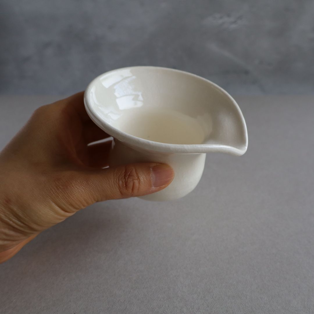 Hand holding a small white ceramic bowl against a neutral background