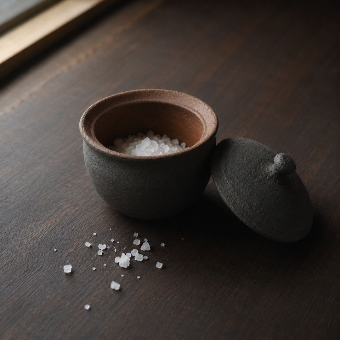 Small ceramic container with lid on a wooden surface, filled with salt.