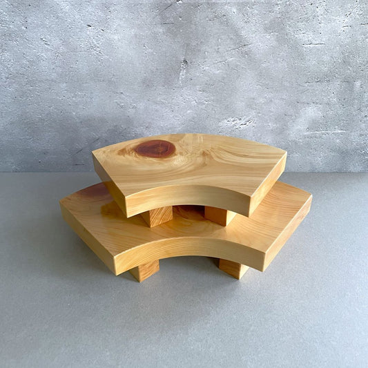 Two tiered wooden sushi serving trays with a smooth finish, stacked on top of each other on a grey surface against a textured wall.