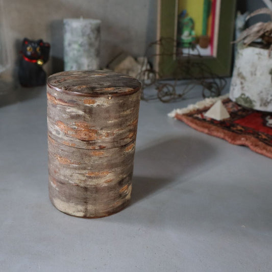 A cylindrical tea caddy made of natural wild cherry bark with a marbled pattern, displayed on a flat surface.