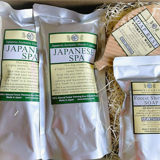 A set of Japanese spa products including two bags of Hinoki Cypress chips, a Hinoki soap bar, and a wooden soap dish, all eco-friendly and made in Japan.