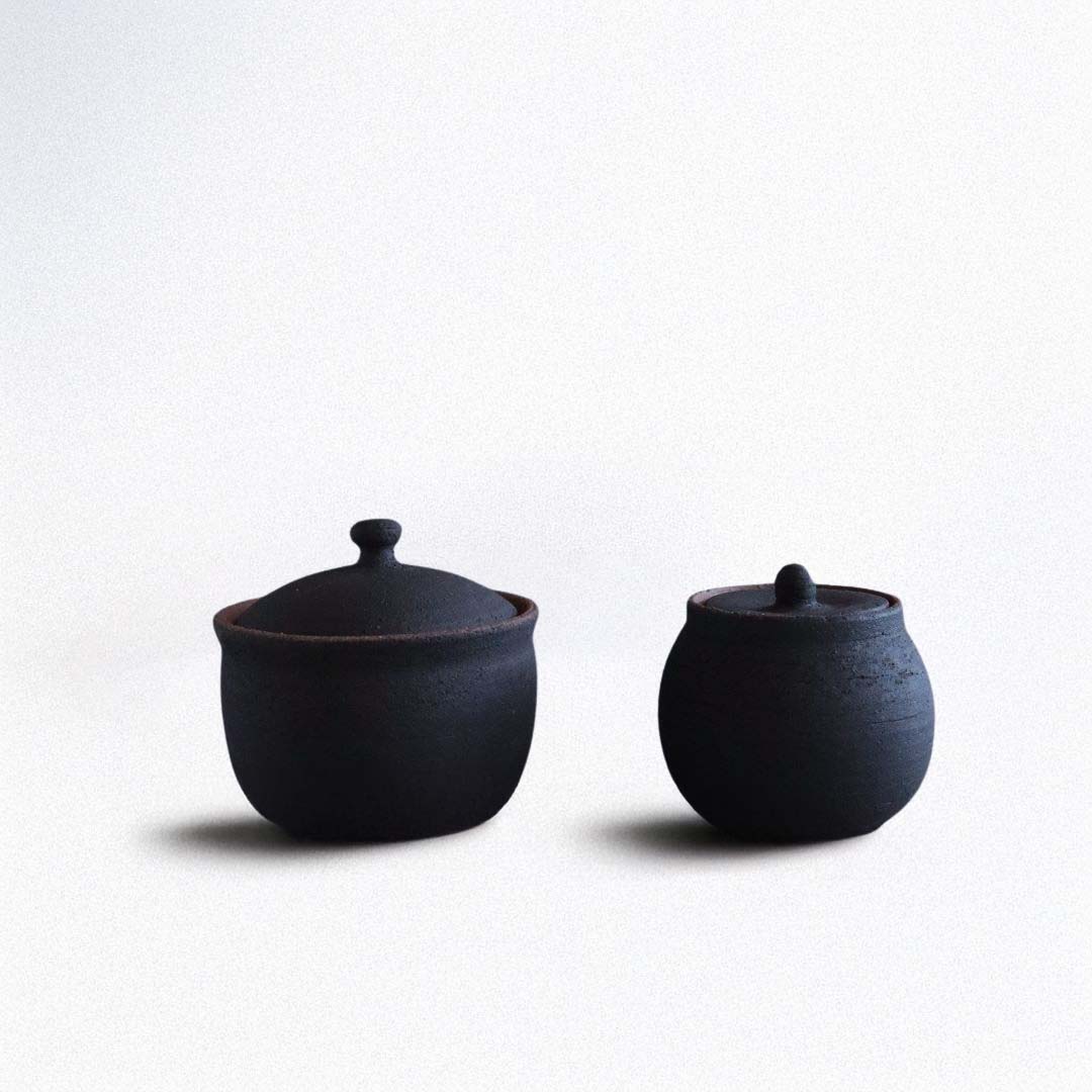 Two handmade black ceramic salt cellars with lids, one larger and one smaller