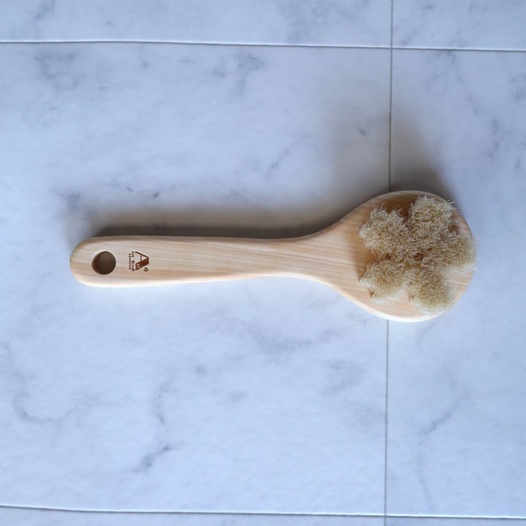 Top view of a Japanese Sakura body brush made from natural Hinoki wood, featuring soft white horsehair bristles shaped like a cherry blossom, designed for gentle exfoliation and spa-quality skincare.