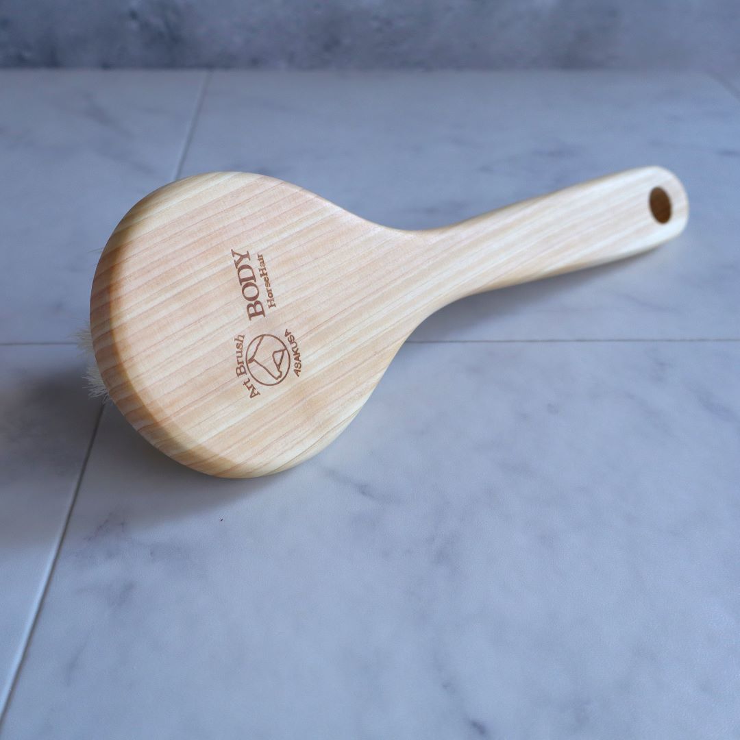 Back view of a Japanese Sakura body brush made from natural Hinoki wood, featuring a smooth, ergonomic handle with engraved branding, designed for gentle exfoliation and spa-like skincare.