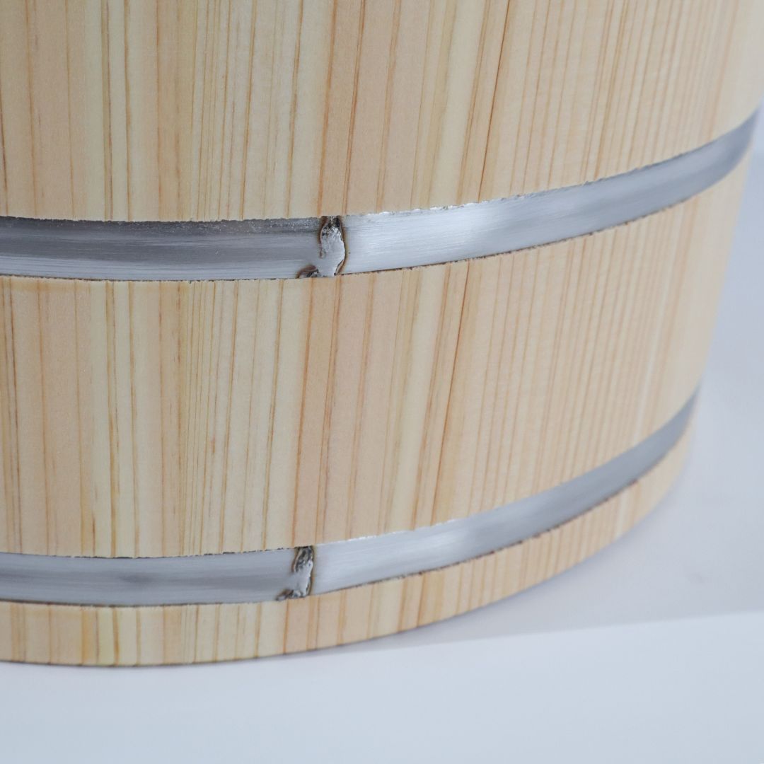 Close-up of a light natural wood cylindrical barrel or bucket with two horizontal silver metal bands around it, photographed on a white background.