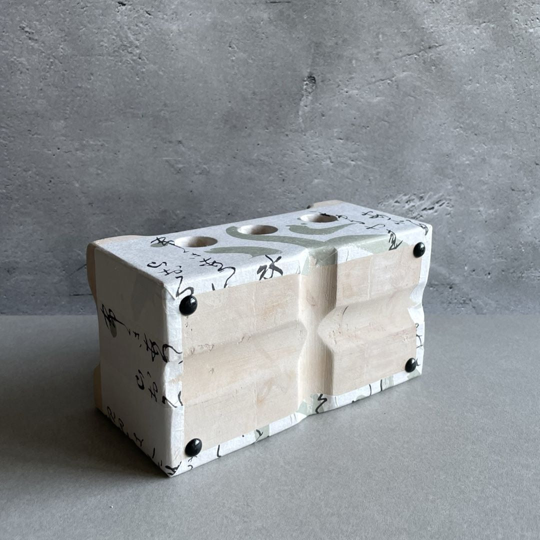 A white square clay table barbecue with ideogram on the side and three holes, lying on its side to show its underside.