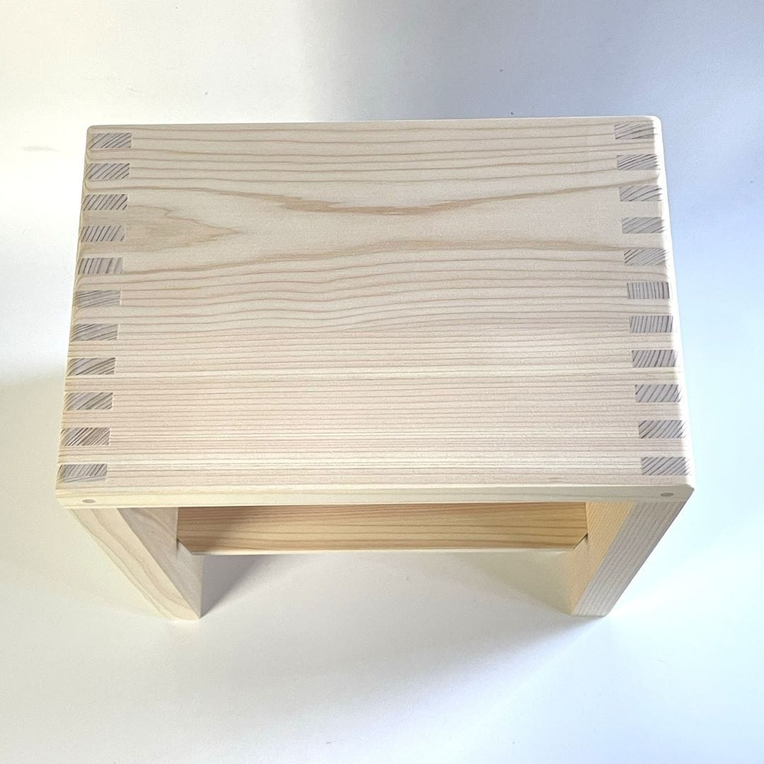 This is a top-down view of a Japanese square wooden shower stool located in the center of a bathroom with faience tiling on the walls. The stool&