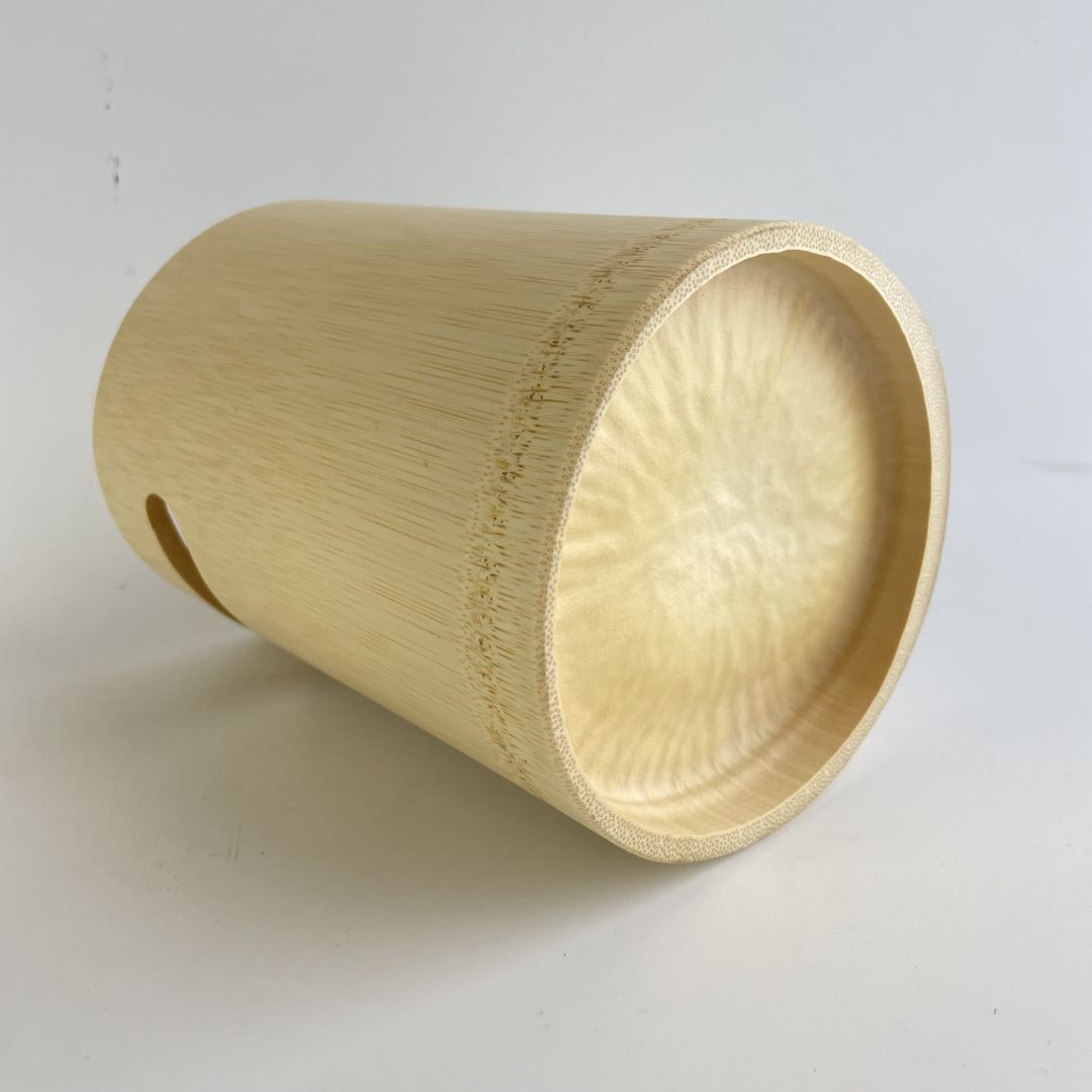 A light wooden bucket is lying on its side against a white background, with a visible handle slot on the nearest side. The bucket displays a natural wood grain texture with a smooth, curved rim. The angle of the image provides a glimpse into the bucket&