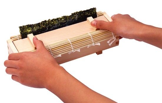 Two hands on each side of a sushi kit maker holding a wooden board on a sushi box