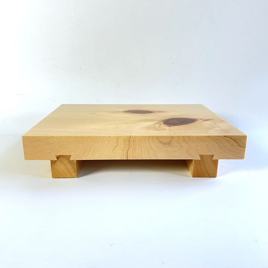 An image of a wooden sushi tray captured in a horizontal view. The tray is placed on a white surface, and the surrounding environment is also white, creating a clean and minimalistic look. The wooden texture of the tray is prominent, featuring natural grains and patterns. The sushi pieces are not visible in this image, but the tray's simple and elegant design is the focal point of the composition.