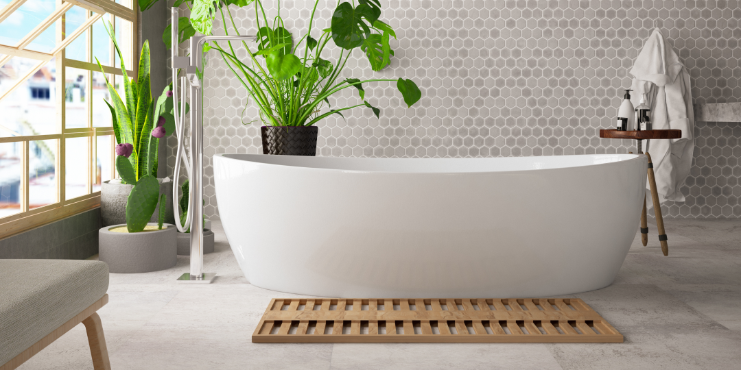 a wite bath next to a wooden bath mat and a green plant in a white bathroom