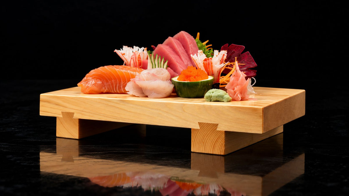 Hinoki wooden sushi tray with assorted sashimi on a black table.