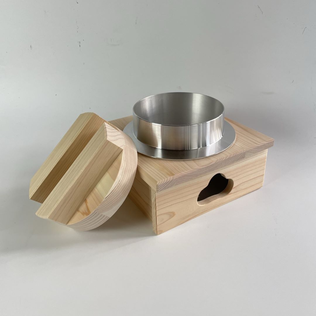 Hagama rice cooker made of hinoki wood, with the lid open, resting on the edge. White grey background accentuates the rustic beauty.