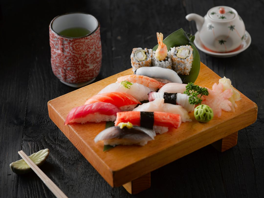 sushi tray with sushi on it next to a cup of green tea and sou sauce
