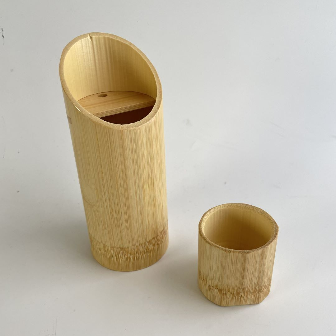 A bamboo sake bottle and a bamboo sake cup standing in a grey room