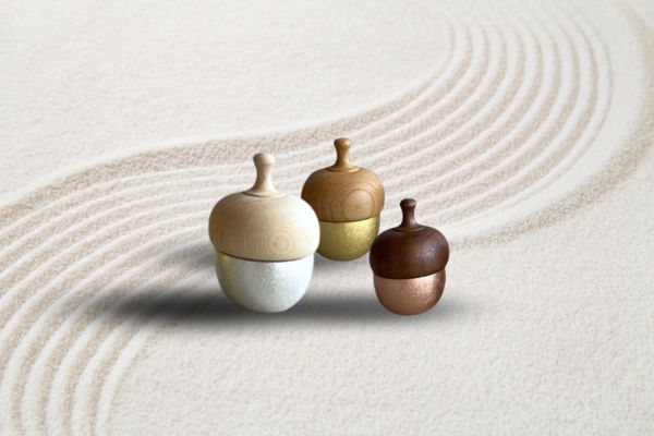 Hand holding a metal bell above a singing bowl on a grey background. The bell and bowl are used for meditation and sound therapy.