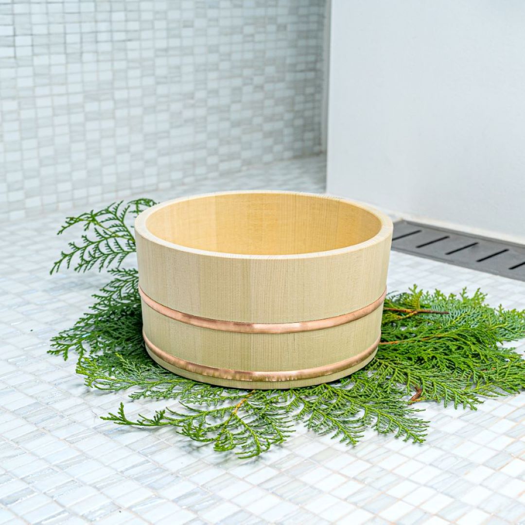 Japanese spa bath bucket made of Hiba wood lay down on a pine tree branches in a white porcelain bathroom