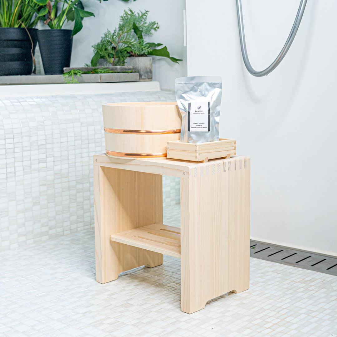 wooden bucket, soap on a wooden soap dish on a wooden square stool in a white porcelain bathroom and green plants in the back