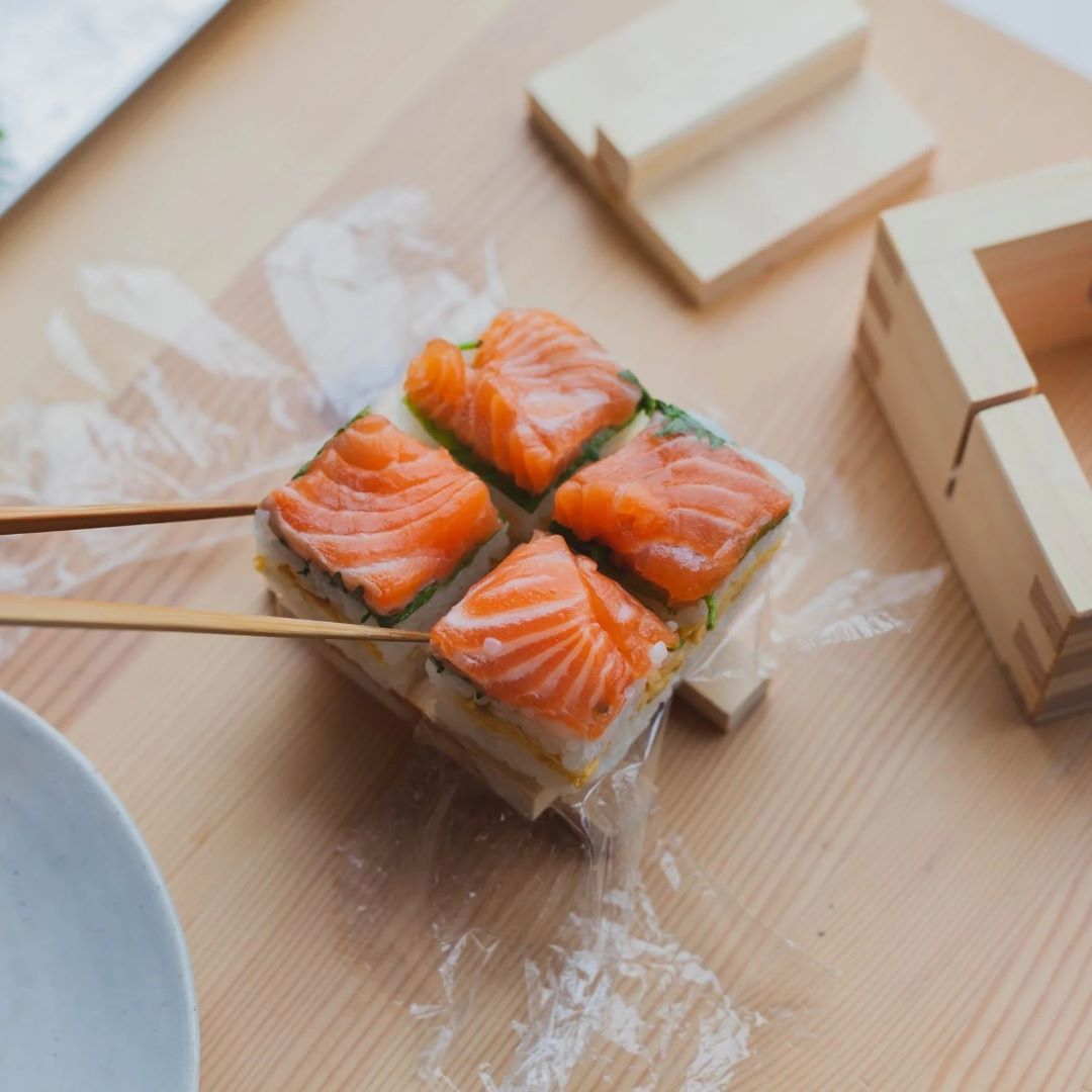 A wooden sushi board on a grey kitchen counter surrounded by green plants
