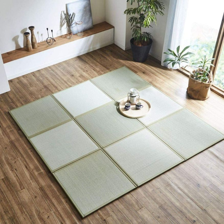 A green tatami square pieces on a wooden floor surrouned by green plants