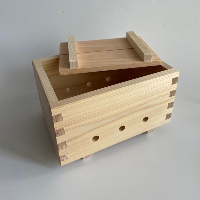 A handcrafted wooden tofu press made from natural white pine wood and uncoated sawara cypress. The box features interlocking corner joints and multiple holes on the sides for drainage. The lid is partially open, showcasing the craftsmanship.