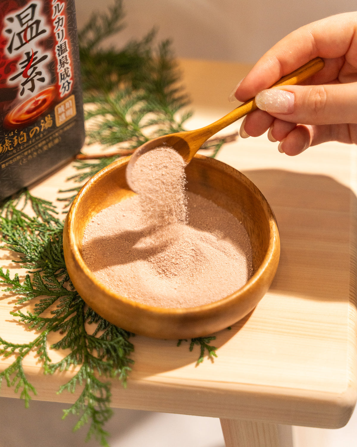 Wooden bowl with powdered substance, wooden spoon, and greenery on a wooden surface.