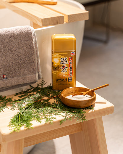 Bottle of tea and wooden bowl with spoon on a wooden stool with towel and greenery